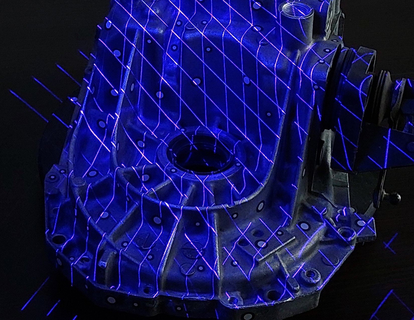 Krzyżujące się niebieskie linie laserowe wyświetlone na powierzchni odlewanego korpusu podczas skanowania 3D.